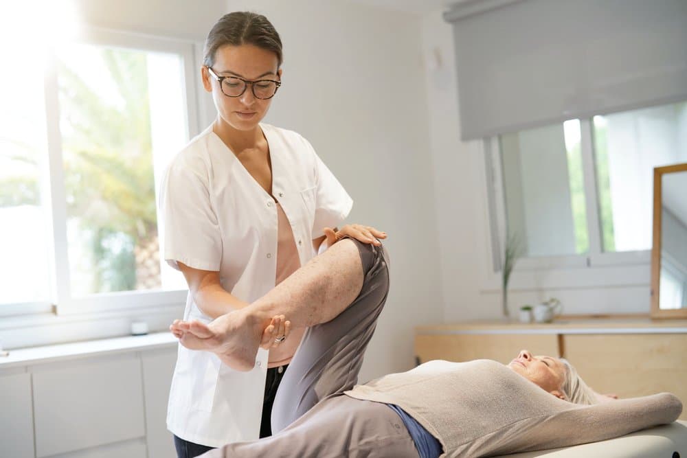 A therapist gently stretching a reclining patient's leg.