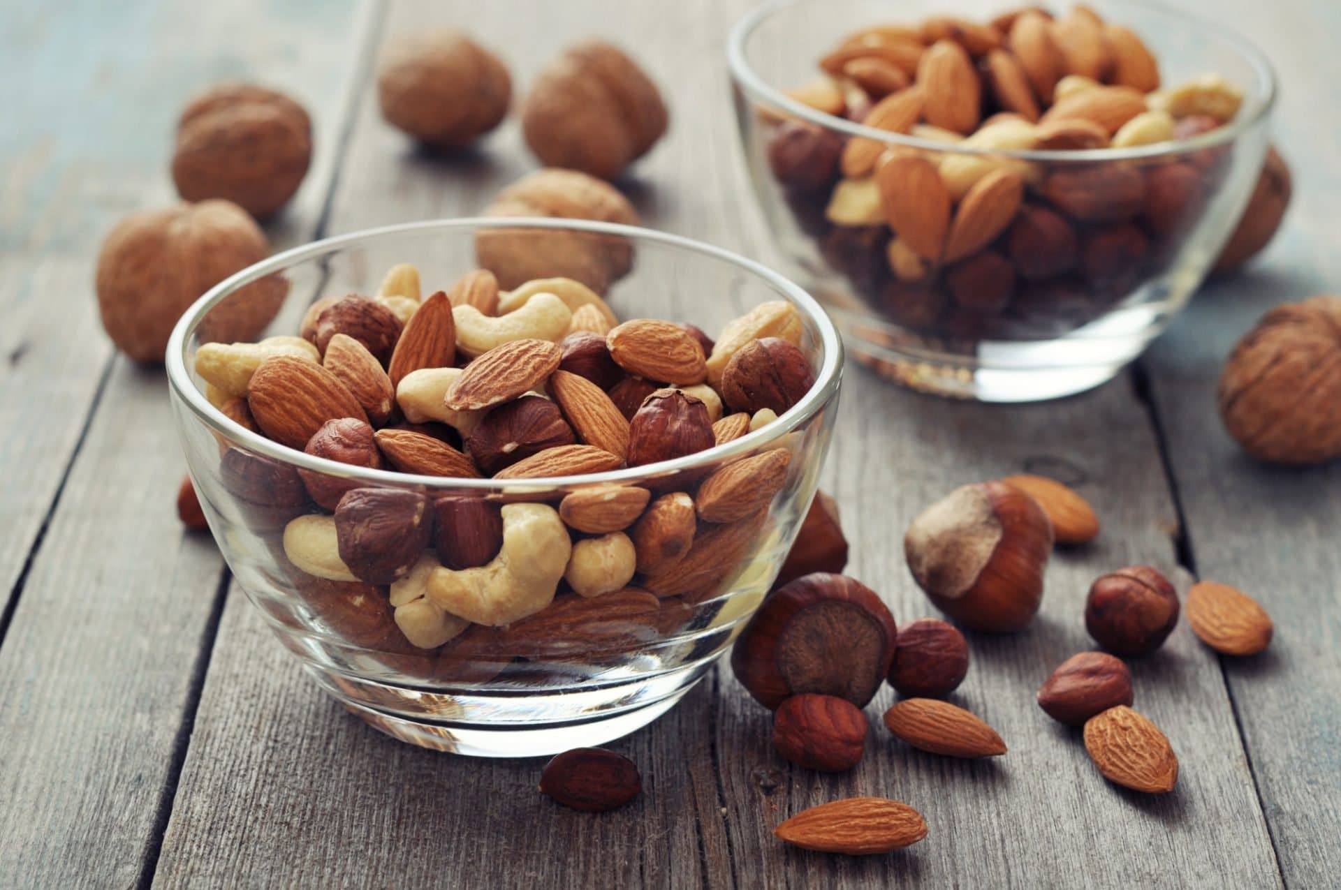 Glass bowls of almonds, walnuts and mixed nuts on a wooden table.
