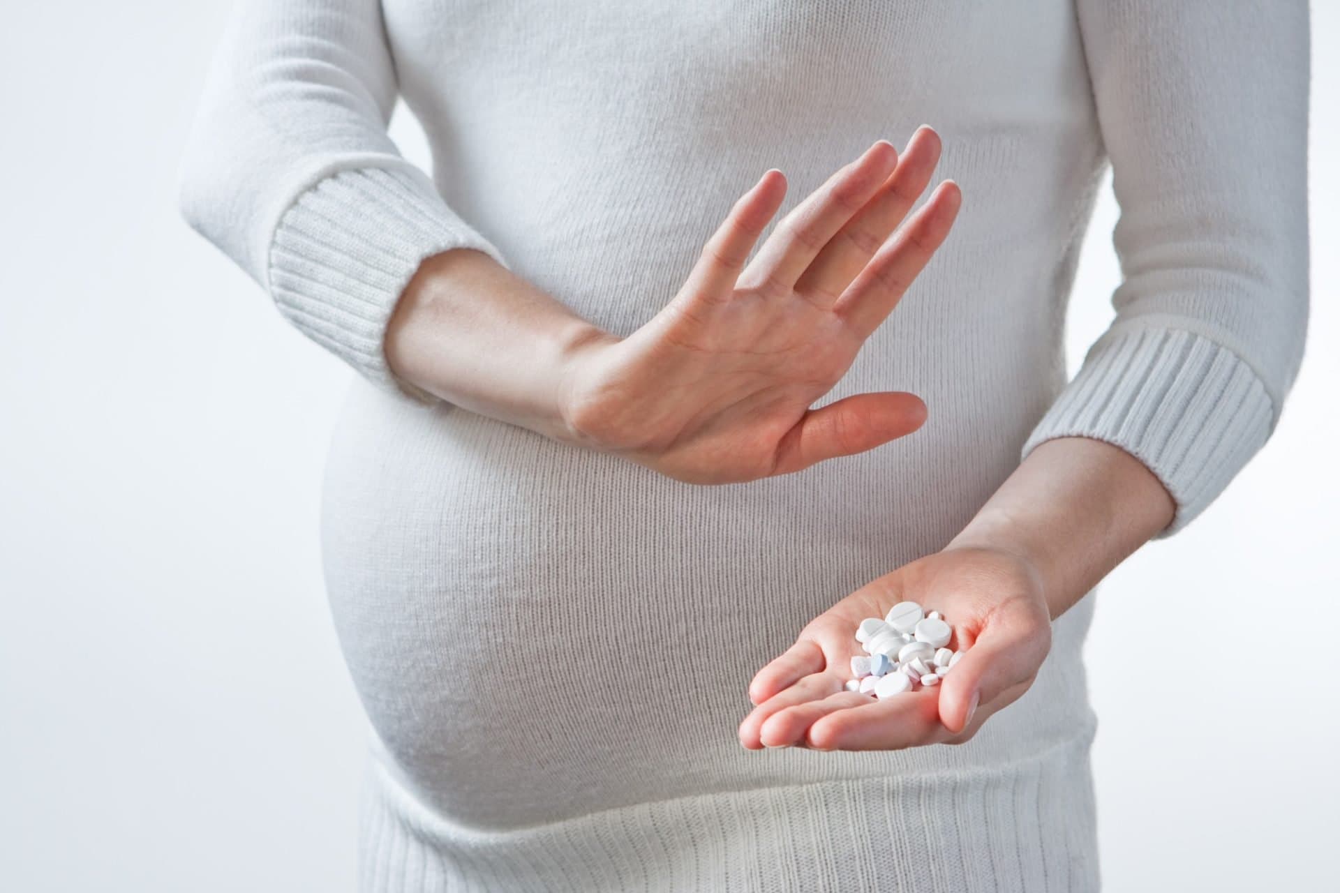 A pregnant woman holding up her hand to decline a handful of pills.
