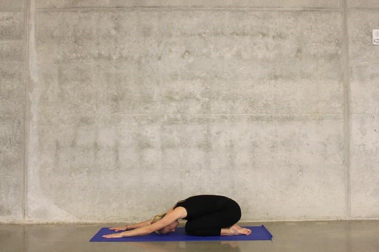 A woman resting in a yoga child's pose on a blue mat.