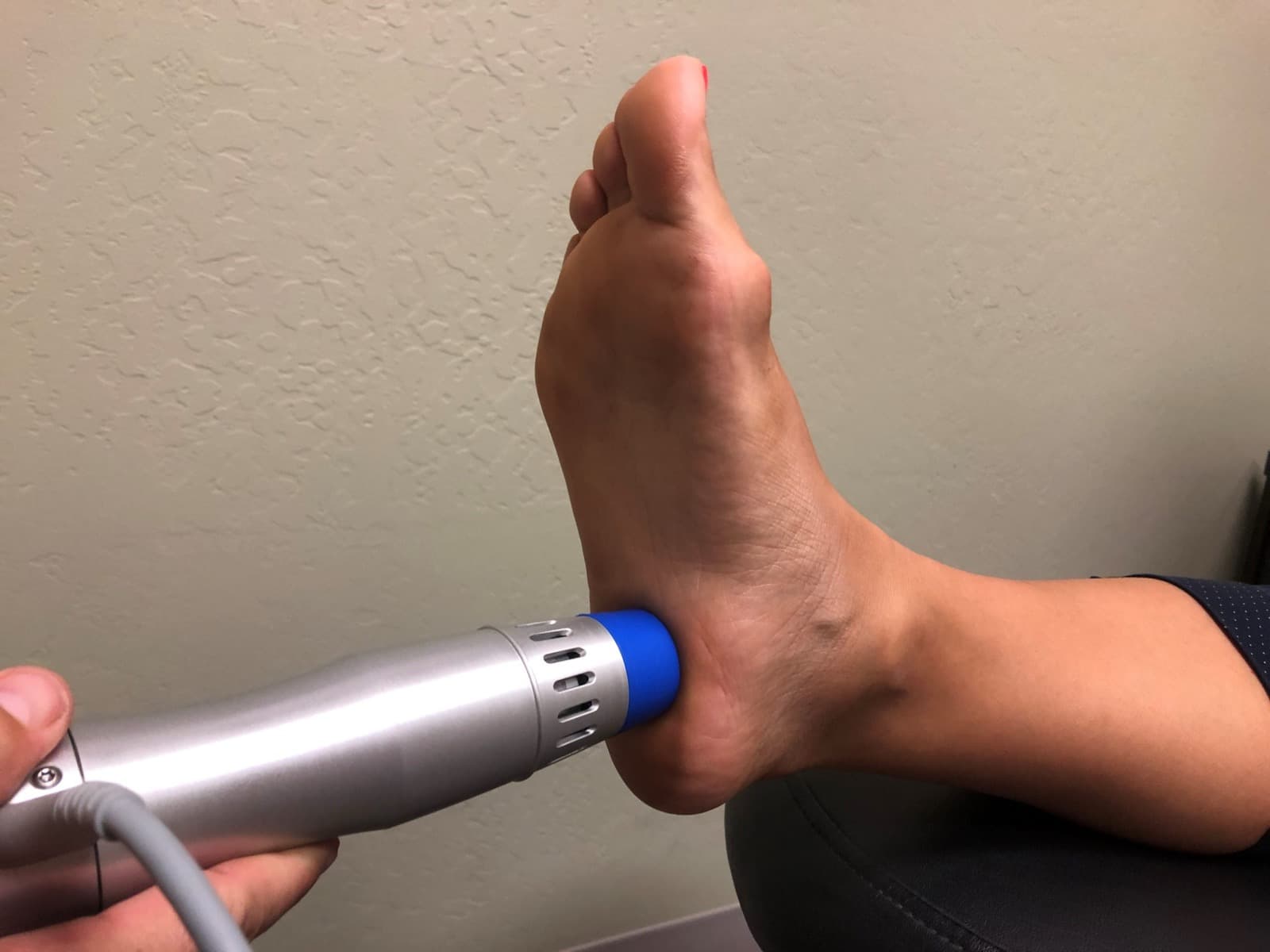 A shockwave applicator held against the back of a patient's heel.